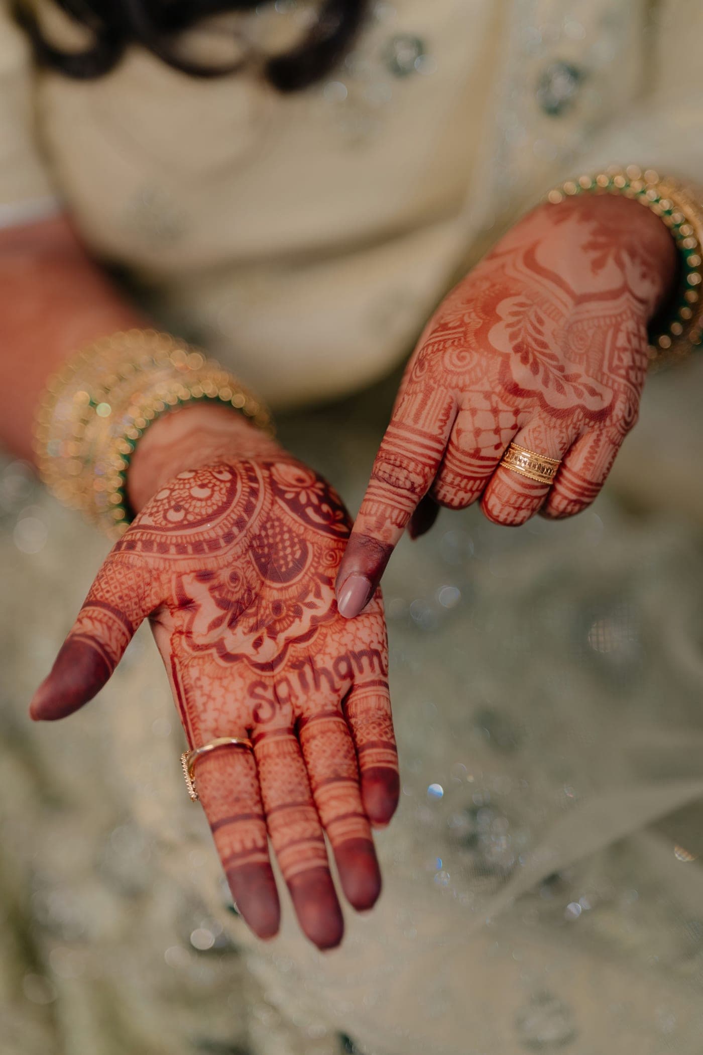Intricate henna patterns on a bride’s hands adorned with gold rings and bangles