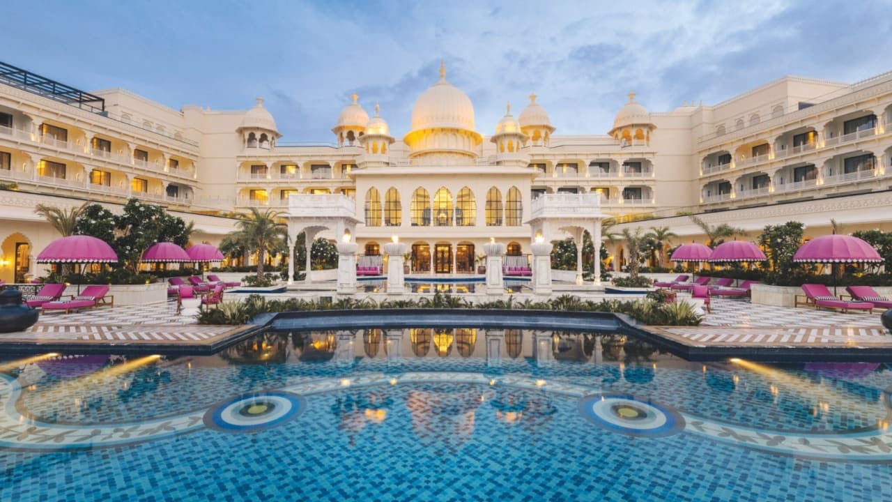 A grand white palace with domes and terraces beside a lake at dusk
